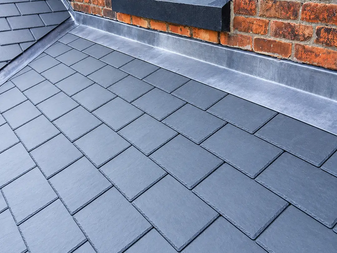 New slate roof with lead flashing finished neatly against a brick wall